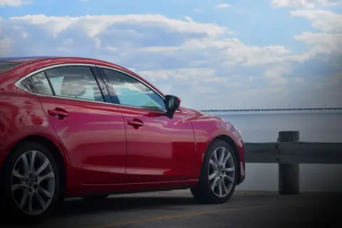 Czerwona Mazda 6 2.0 benzyna zaparkowana nad wodą, z mostem w tle.