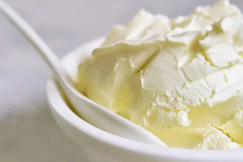 Kremowa masa w białej miseczce z łyżką. Szukasz, czym zastąpić mascarpone? Oto puszysta alternatywa.