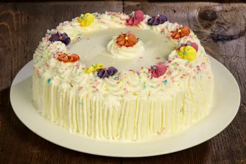 Torta compleanno uomo con panna, decorata con fiori colorati e codette, pronta per festeggiare.