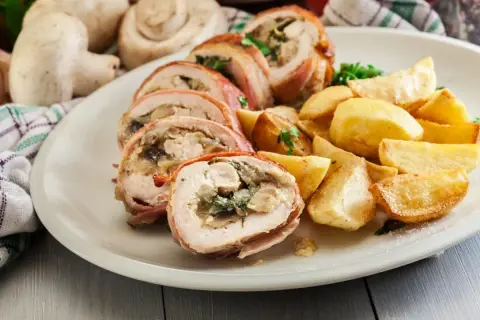 Roladki z kurczaka zawinięte w boczek, podane z pieczonymi ziemniakami i ziołami.