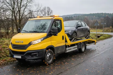Żółta laweta Iveco z ciemnym samochodem na platformie. Zastanawiasz się, ile kosztuje laweta?