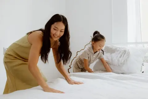 Mutter und Kind machen das Bett frisch. Der Boxspringbett Topper wellt sich leicht, während sie die Bettwäsche glattziehen.
