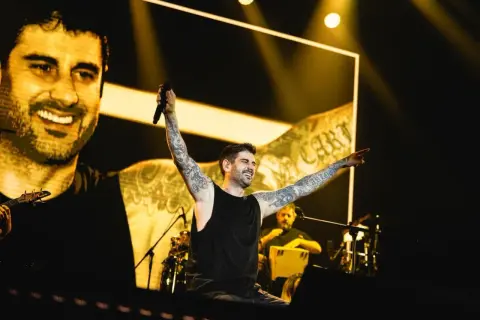 Melendi en concierto en Zaragoza, con los brazos en alto y sonriendo, ante una multitud.