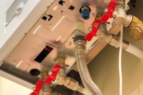 Dettaglio di valvole rosse e tubi di una caldaia, utili per capire come abbassare pressione.