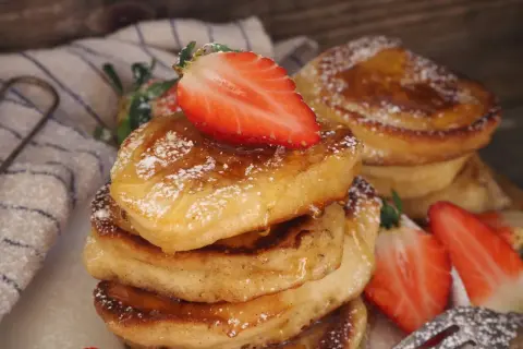 En stapel fluffiga pannkakor på filmjölk, toppade med färska jordgubbar och pudersocker.