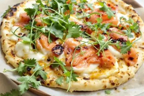 Pizza saumon avec fromage fondant, garnie de coriandre fraîche et d'une touche de piment. Un délice visuel et gustatif.