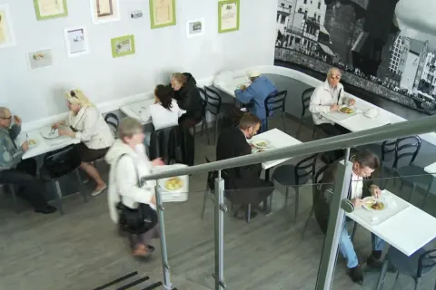 Wnętrze baru turysta. Ludzie jedzą przy stolikach, jeden z nich niesie tacę z jedzeniem.