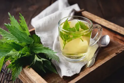 Aromatyczne picie pokrzywy w szklance, obok świeże liście na drewnianej tacy.