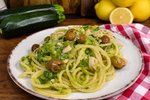 Un piatto invitante di pasta con zucchine e tonno, condita con olive e un tocco di limone.