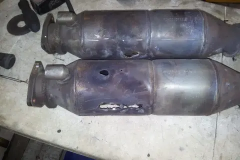 Dos catalizadores de coche rotos, con agujeros visibles, evidencian porque se rompe el catalizador del coche por sobrecalentamiento o golpes.