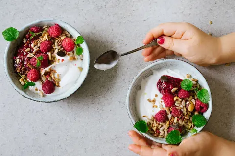 Två skålar med kokosyoghurt, hallon, granola och mynta. Perfekt för ett enkelt kokosyoghurt recept.