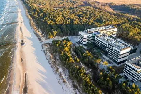 Nowoczesne budynki hotelowe w Rogowie nad morzem, otoczone sosnowym lasem, z widokiem na piaszczystą plażę i fale Bałtyku.