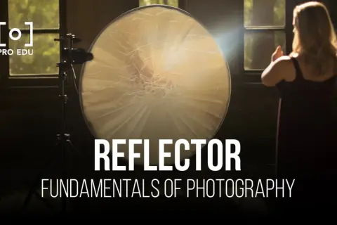 A large, round reflector is used to bounce light in this photography setup. A woman stands in the background, her hands raised.