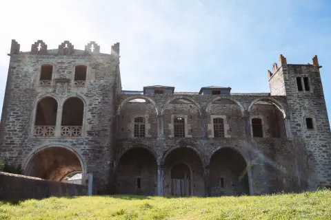 El imponente castillo de Arnado, con sus arcos y torres de piedra, se alza sobre un prado verde bajo un cielo azul.