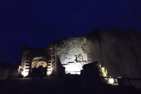 Nuit tombante sur un château abandonné dans la Somme. Des lumières éclairent l'entrée voûtée et les vieilles pierres.