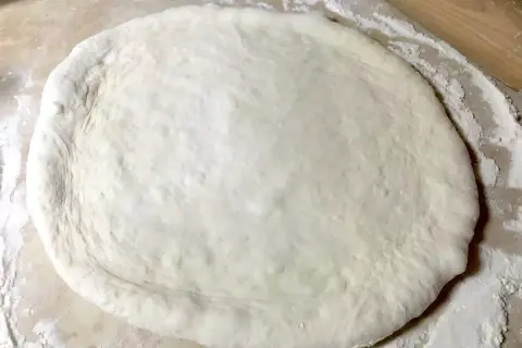 Pâte à pizza moelleuse étalée sur un plan de travail fariné, prête pour la recette.