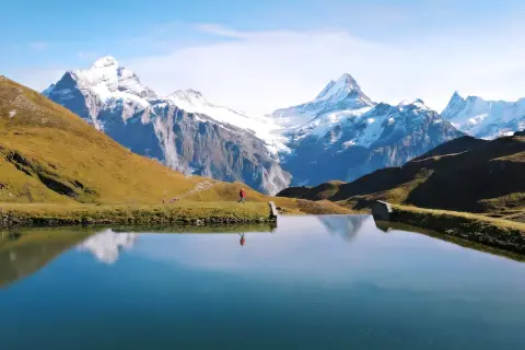 Osoba w czerwonej kurtce spaceruje nad jeziorem w Grindelwald, podziwiając ośnieżone szczyty Alp.