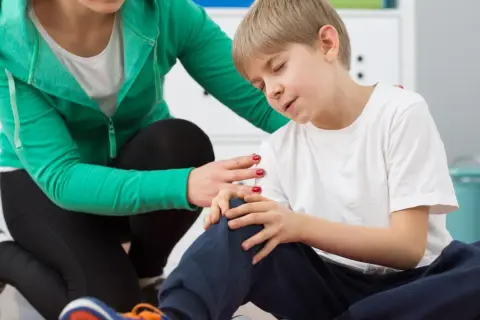 Fizjoterapeuta pociesza chłopca z bólem kolana.