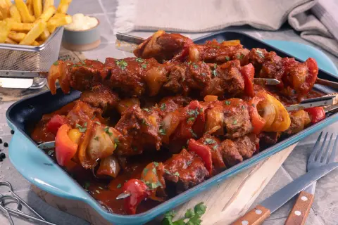 Herzhaftes Schaschliktopf Rezept: Fleischspieße mit Paprika und Zwiebeln in würziger Tomatensauce, serviert mit Pommes.
