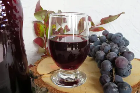 Ciemnoczerwone wino w kieliszku, obok kiść winogron i butla. Idealne do domowego wina w 5 litrowej butli.