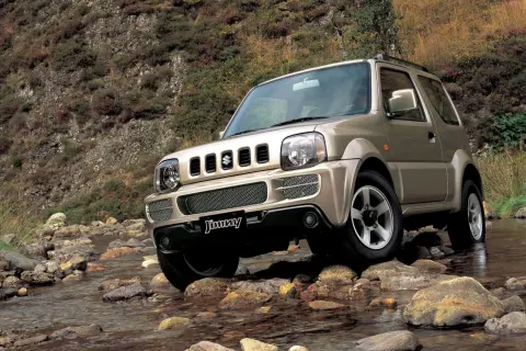 Złoty Suzuki Jimny (1998) pokonuje kamienisty strumień, gotowy na każdą przygodę.