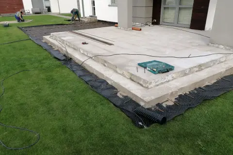 Budowa tarasu z betonu. Pracownicy przygotowują teren pod nową nawierzchnię, układając zbrojenie i materiały izolacyjne.