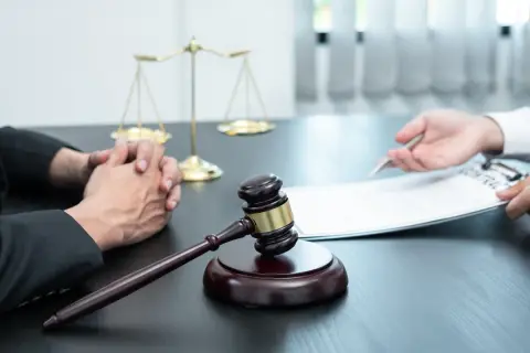 Sądowy młotek i waga sprawiedliwości symbolizują proces, który może prowadzić do wydziedziczenia. Dwie osoby przy stole, jedna z dokumentami, druga z rękami złożonymi w geście niepewności.