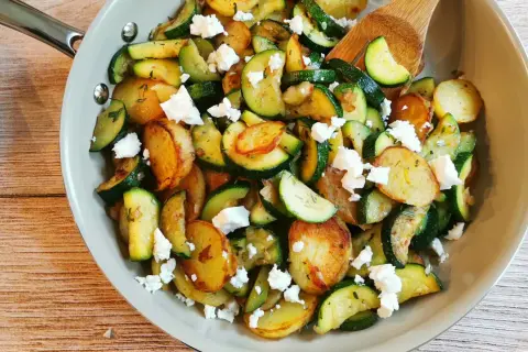Herzhafte zucchini pfanne mit goldbraunen Kartoffelscheiben und zerbröseltem Feta, garniert mit frischen Kräutern.