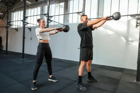 Para, co to jest crossfit, wykonuje ćwiczenie z kettlebell. Intensywny trening buduje siłę i wytrzymałość.