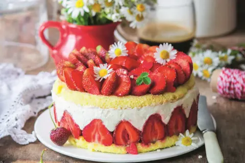 Puszysty biszkopt z truskawkami i mascarpone, ozdobiony świeżymi owocami i stokrotkami. Idealny na letnie popołudnie.