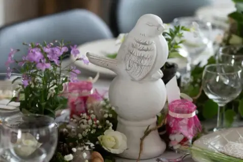 Décoration champêtre pour un baptême civil : figurine oiseau, fleurs, bougies roses et petits pots garnis.