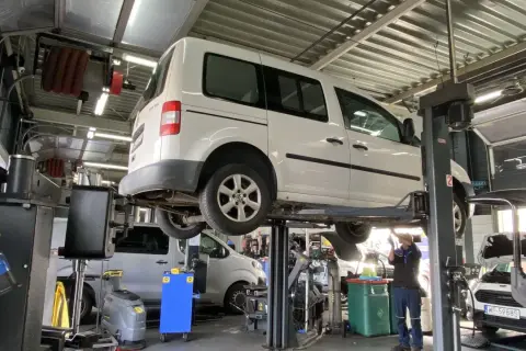 Warsztat samochodowy. Mechanik pracuje pod białym vanem na podnośniku. Prawdziwe powody dla których serwisy odmawiają montażu części dostarczonych przez klienta.