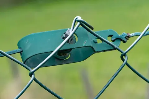 Grüner Drahtspanner hält den Maschendrahtzaun straff.