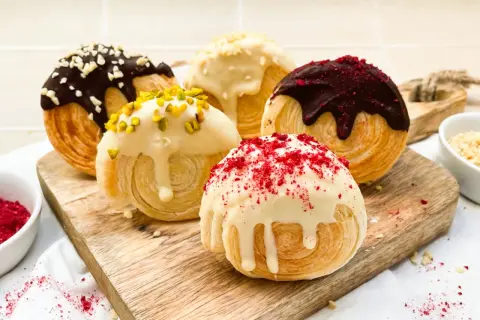 Fünf köstliche New York Rolls, verlockend mit Schokolade, Pistazien und roten Streuseln verziert, auf einem Holzbrett.