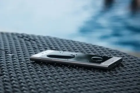 Smartfon z kroplami wody na ekranie, leżący na plecionej powierzchni. To dowód, że IP68 co oznacza – pełną ochronę przed pyłem i zanurzeniem w wodzie.