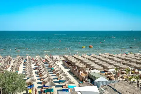 Słoneczne rumuńskie wakacje nad Morzem Czarnym. Plaża pełna leżaków i parasoli, ludzie kąpią się i relaksują.