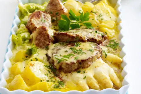 Herzhafte Spargelgerichte mit Fleisch: zarte Medaillons auf Kartoffeln und Spargel, überbacken mit Käse und garniert mit Petersilie.