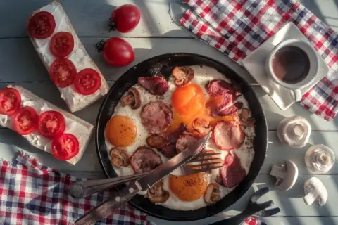 Pyszne polskie śniadanie: jajecznica z kiełbasą i grzybami, kanapki z pomidorami i kawa.
