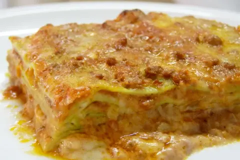 Une part de lasagne généreuse, aux couches de pâtes, sauce bolognaise et béchamel, évoquant la richesse de la lasagne origine.