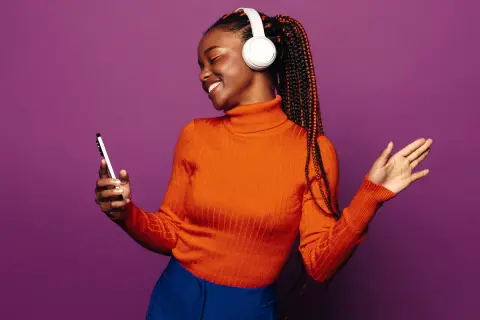 A woman with braids and headphones smiles, holding a phone. She's a visual representation of how to get your music on playlists.