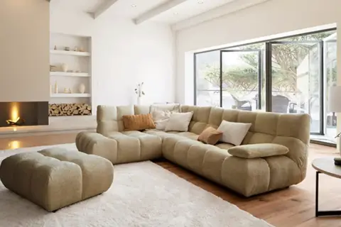 Gemütliches Wohnzimmer mit großem Ecksofa, Kamin und Blick in den Garten – ein Ausblick auf die wohntrends 2026.