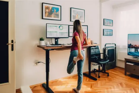Une femme s'étire près d'un bureau réglable en hauteur, parfait pour faire un bureau avec un plan de travail ergonomique.