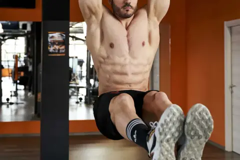 Uomo con addominali bassi scolpiti, appeso a una sbarra in palestra, con focus sui muscoli addominali.