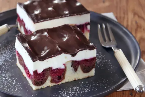 Zwei Stücke saftige Donauwelle mit Kirschen, weißer Creme und Schokoladenguss auf einem Teller. Ein köstliches Donauwelle Rezept!