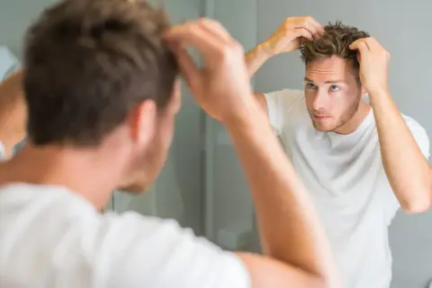 Ein Mann mit strohigem Haar stylt sich vor dem Spiegel.
