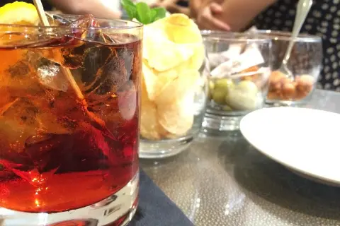 Czerwony drink z lodem i cytryną, obok chipsy i oliwki. Idealny na letnie wieczory, jak z przepisu na absynt.