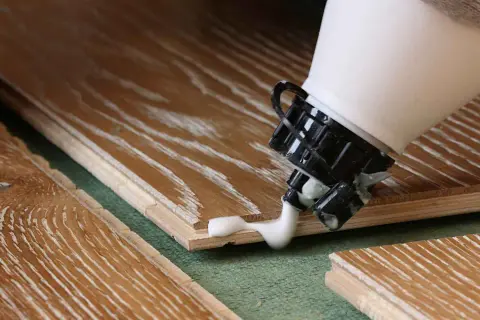 Application de colle sur du bois stratifié. Pour savoir comment enlever de la colle sur du bois stratifié, il faut agir vite.