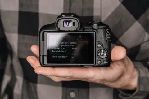 Dłoń trzyma aparat, na ekranie menu. Minimalizm w fotografii to sztuka uchwycenia esencji.