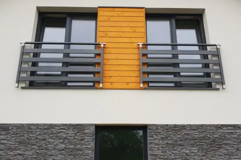 Nowoczesny portfenetr z drewnianym akcentem i ciemną balustradą. Poniżej kamienna okładzina.