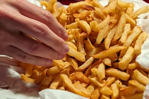 En hand plockar en gyllene pommes frites ur en stor hög med krispiga pommes frites.